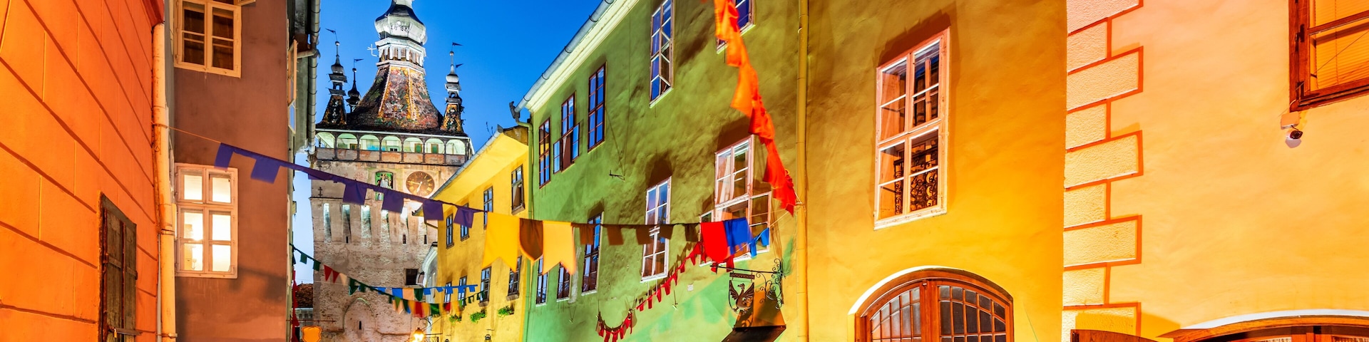 A cobblestone street lined with colorful buildings, a church spire, and flags.