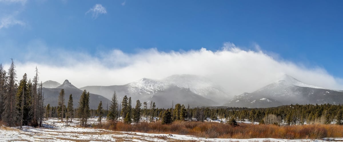 A snowy landscape with a church, mountains, and a forest.