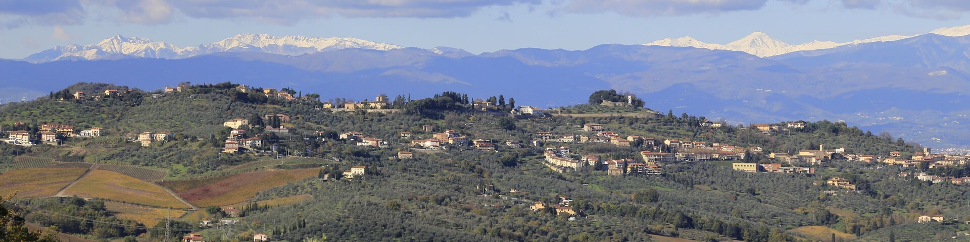 A mountainous landscape with scattered villages, olive groves, and snow-capped peaks in the distance.