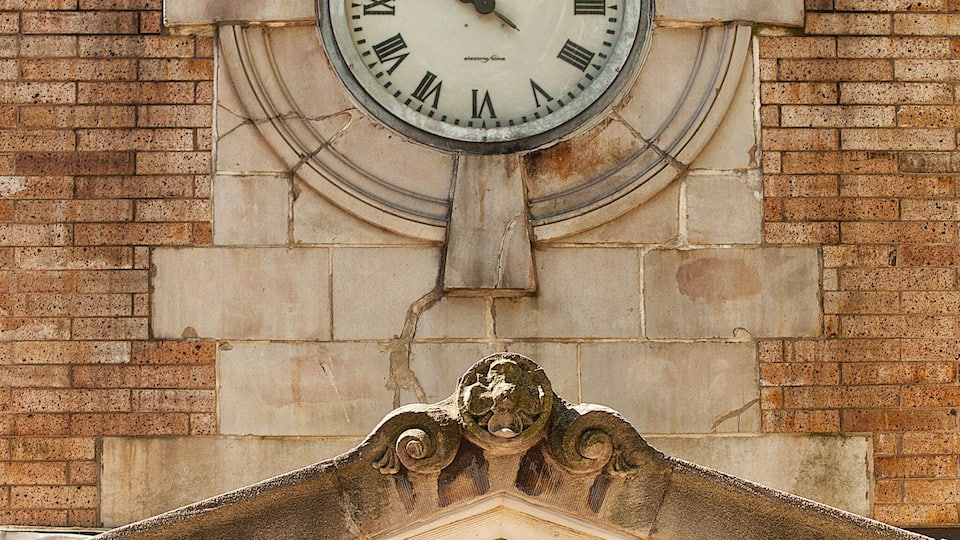 A clock with Roman numerals on a stone building, surrounded by decorative elements and a sign indicating "Bowling Green."