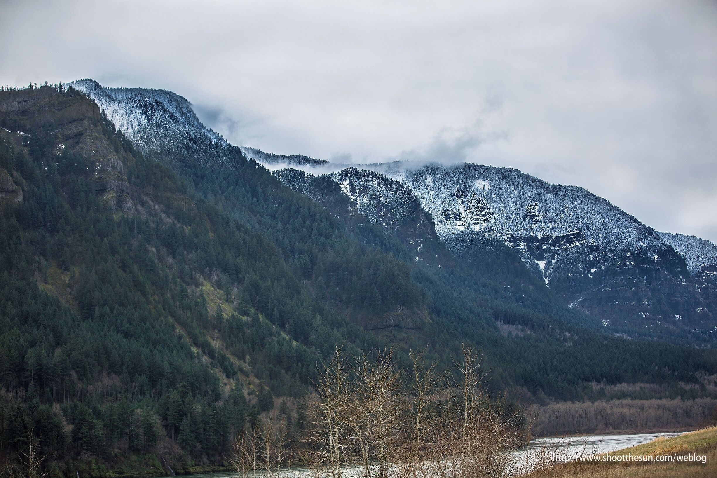 A mountainous landscape with snow-covered peaks and a river in the foreground.