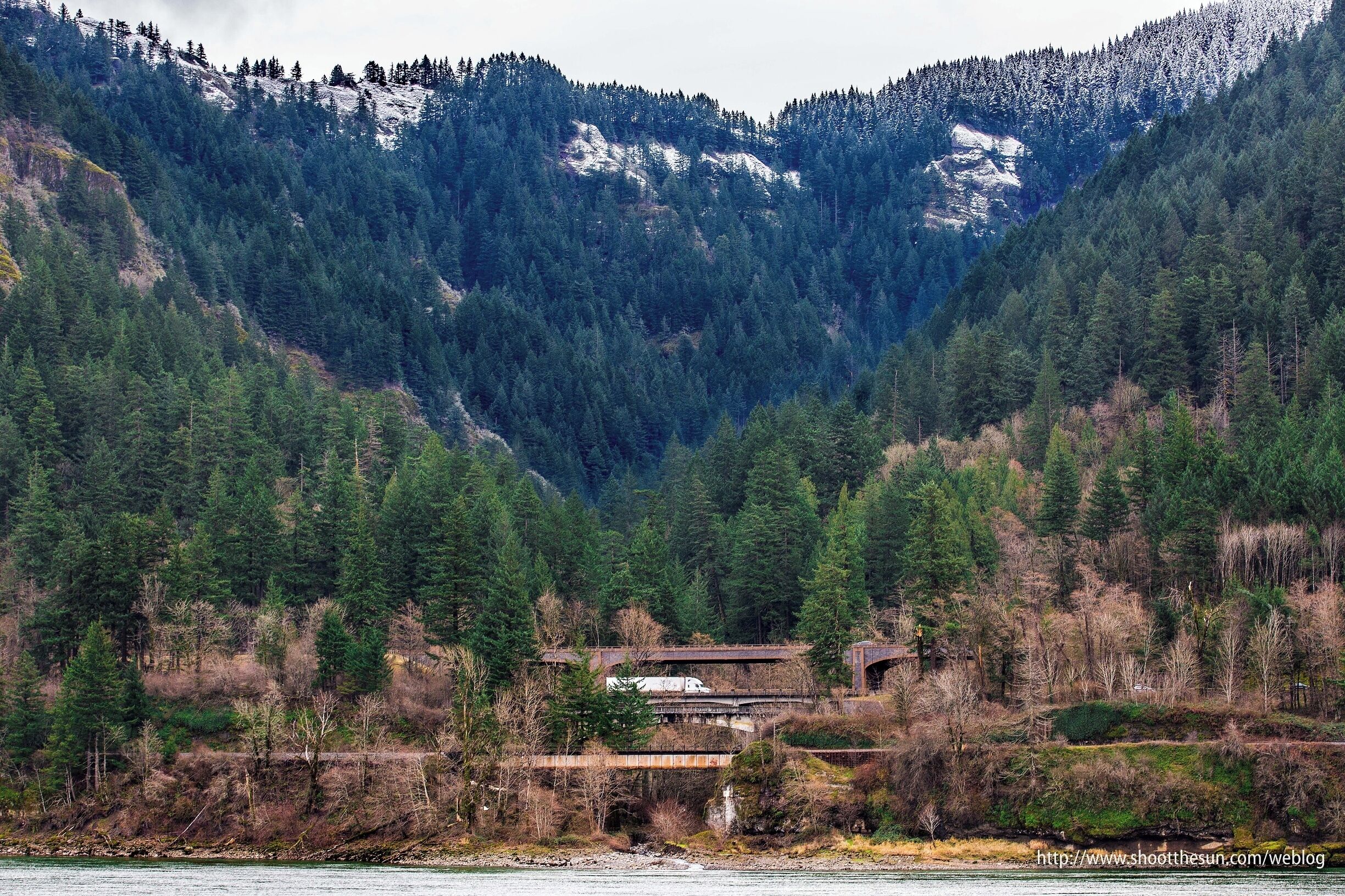The two levels of Interstate I-84, east and west-bound along with a railroad bridge appear briefly through the cleft between a pair of mountains on the Oregon side of the Columbia River.