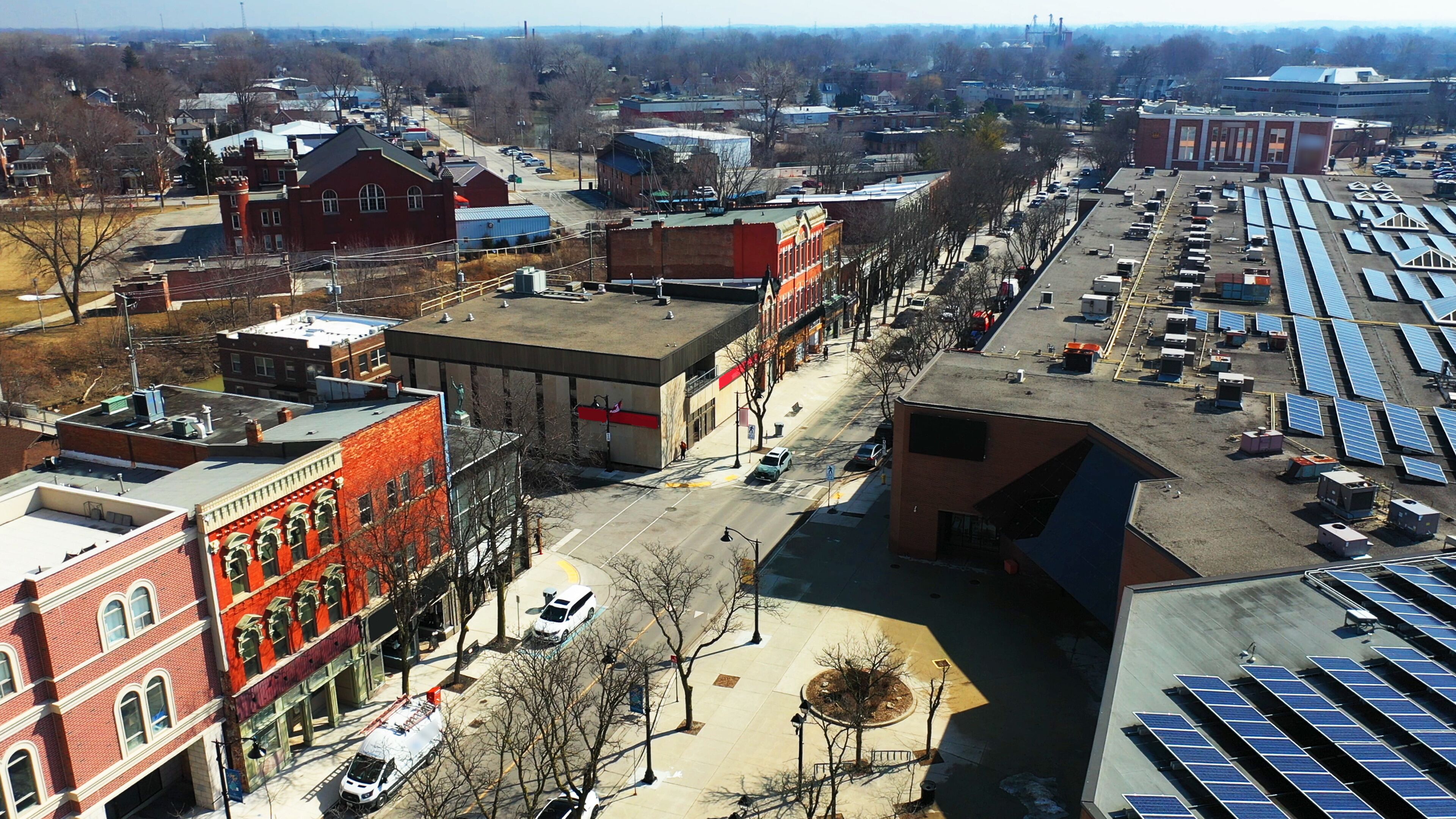 A city street with buildings, parked cars, and solar panels.