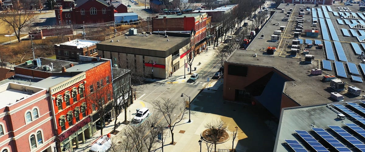 A city street with buildings, parked cars, and solar panels.