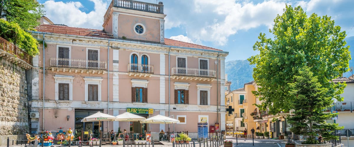 A historic building with a clock tower, outdoor seating, and a mountain backdrop.