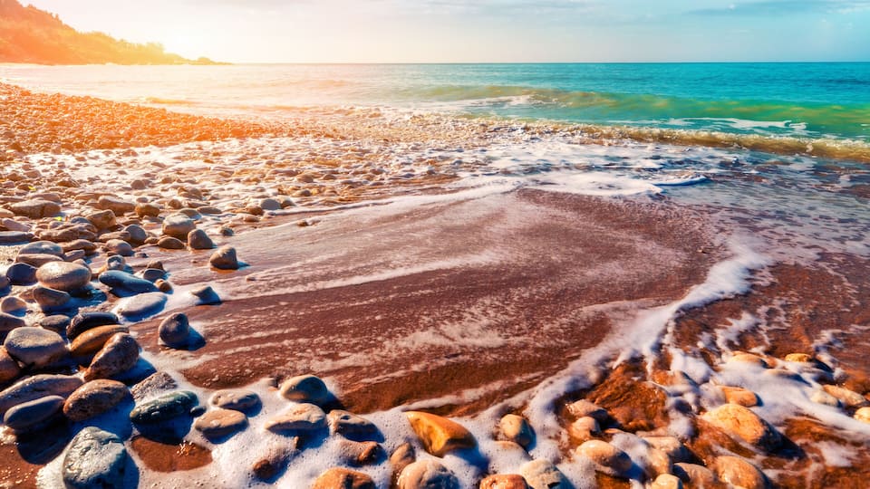 A rocky beach with waves, clear sky, and distant mountains.