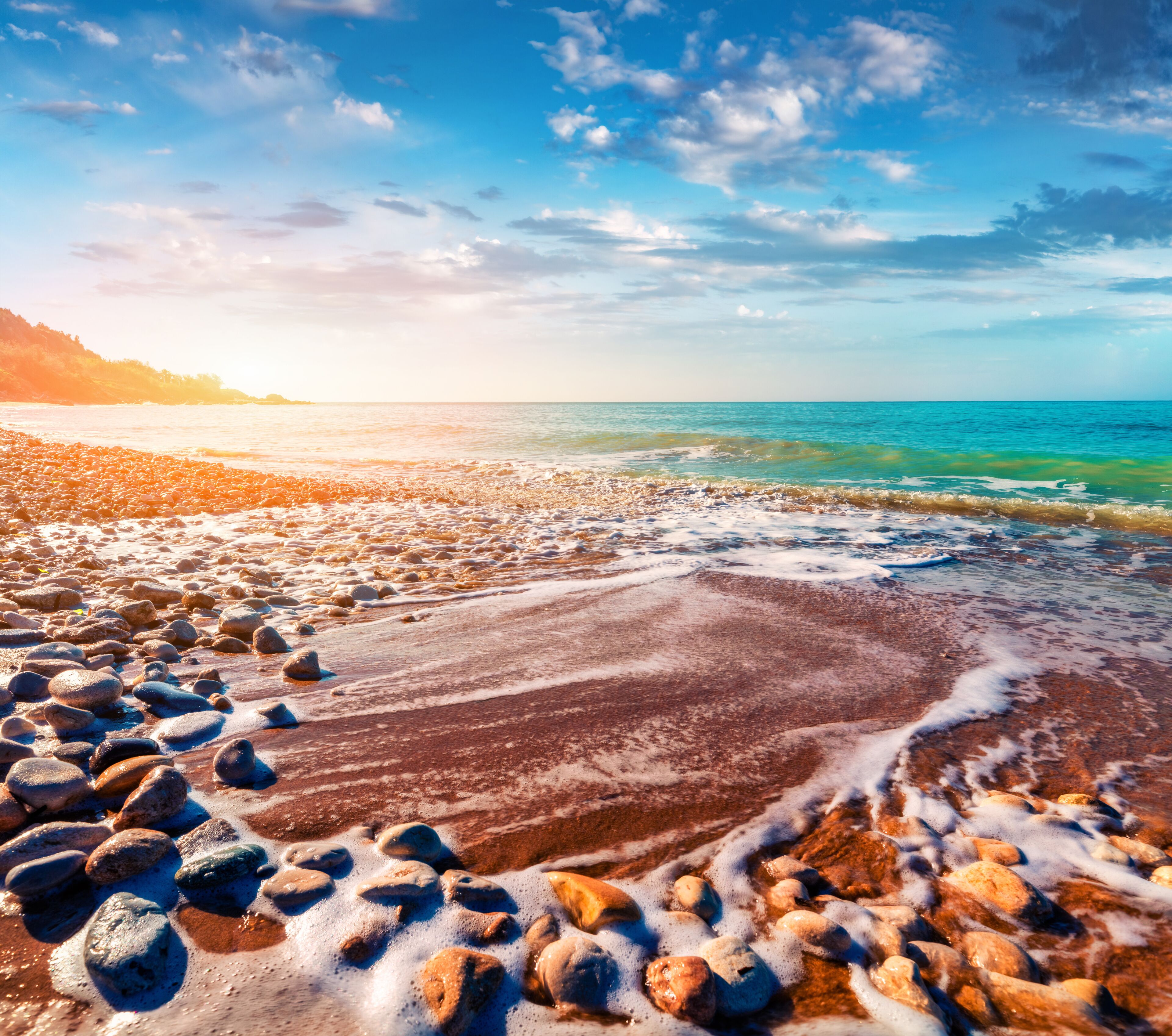 A rocky beach with waves, clear sky, and distant mountains.