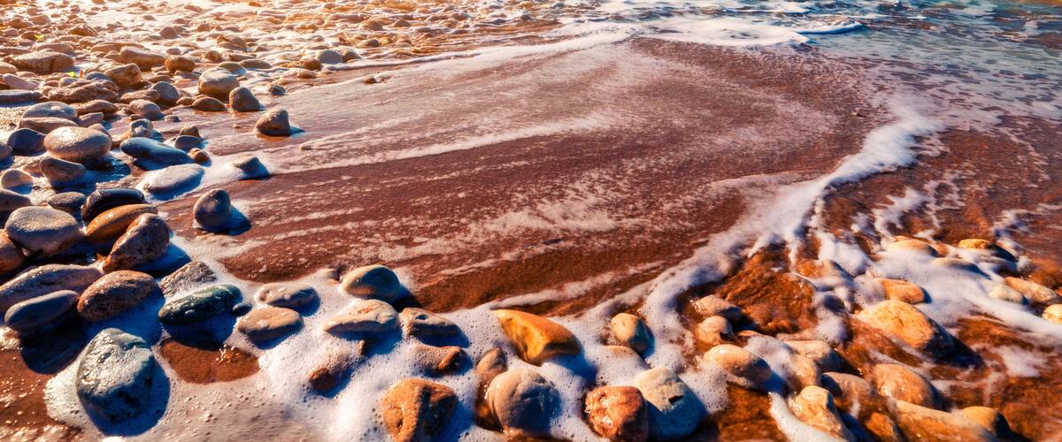 A rocky beach with waves, clear sky, and distant mountains.