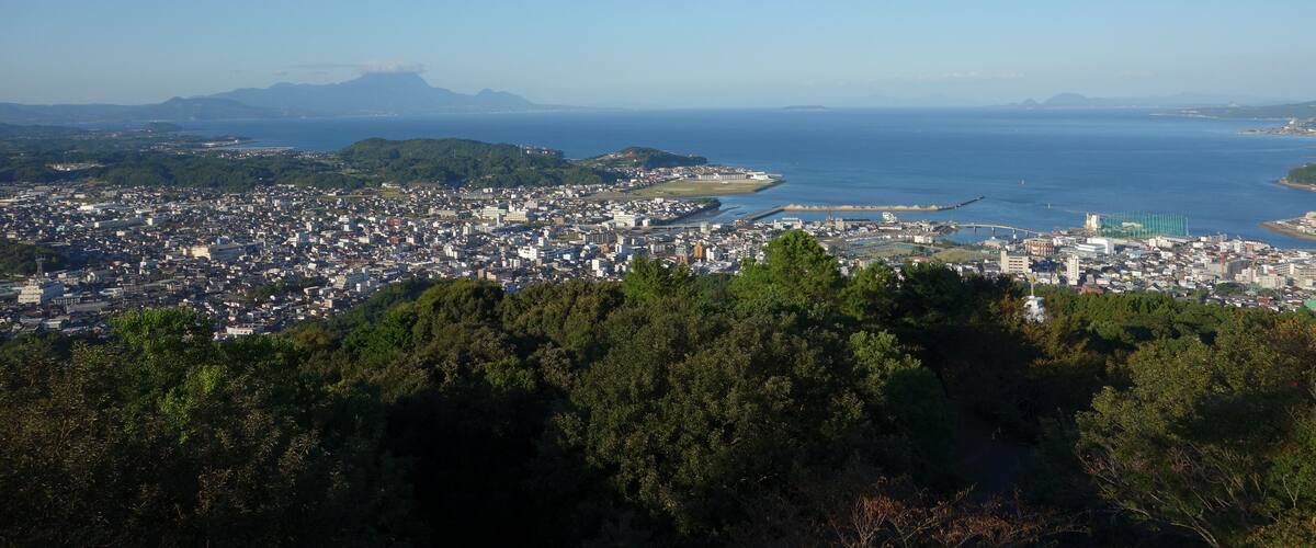 A coastal cityscape with a dense urban area, a large body of water, and distant mountains.