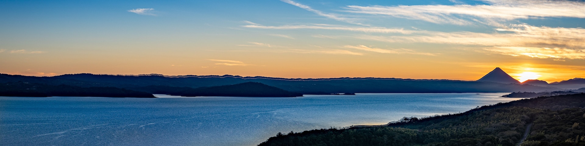 A sunset over a calm lake with distant mountains and a clear sky.