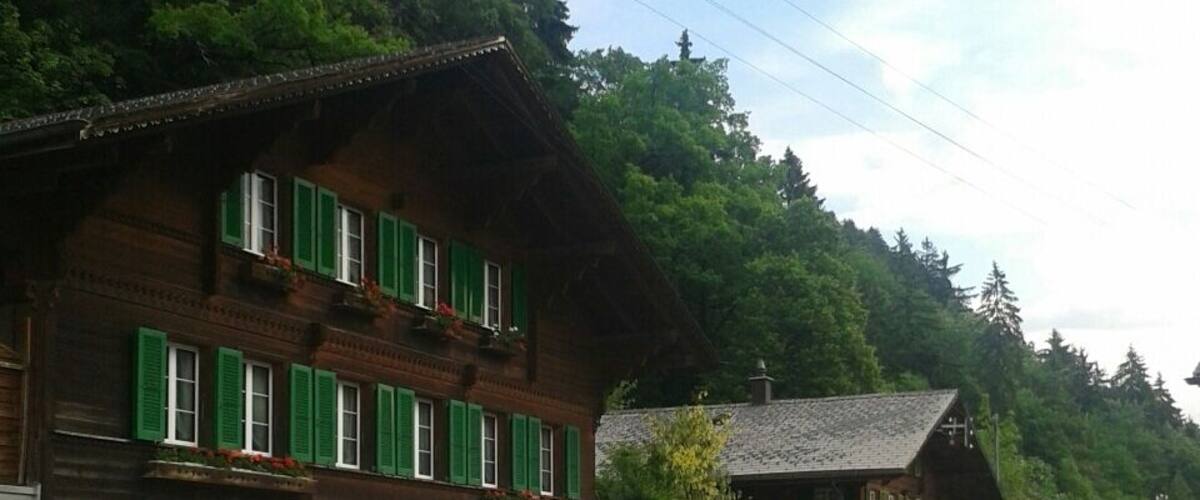 A rural street with traditional wooden buildings, a small shop with green shutters, and a mountain backdrop.