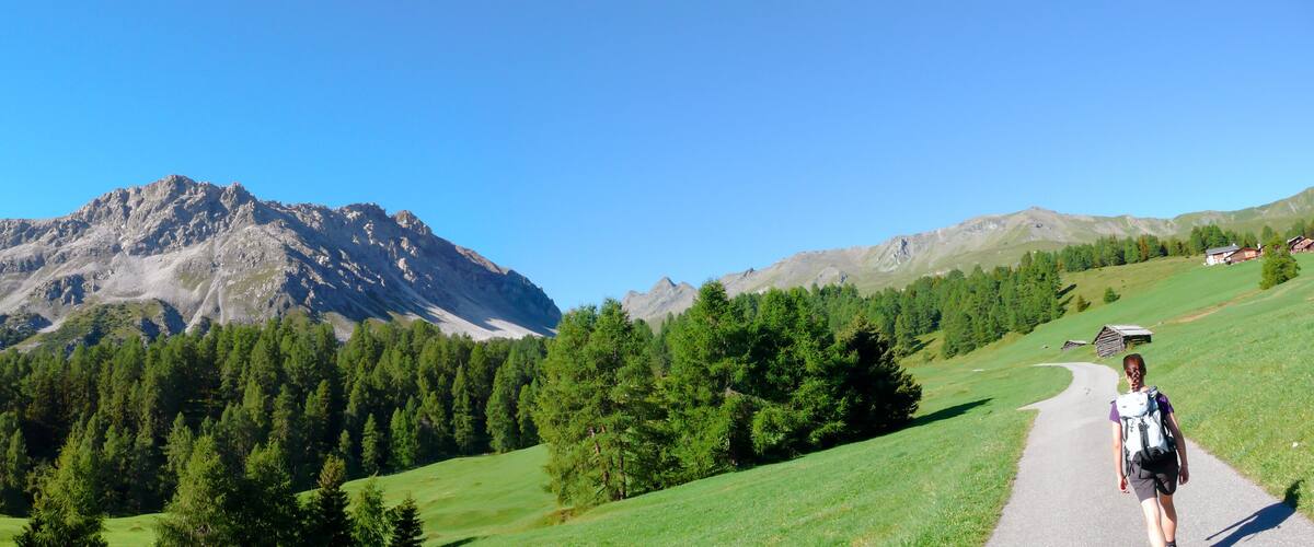 A mountainous landscape with a clear sky, a trail, and a person hiking.