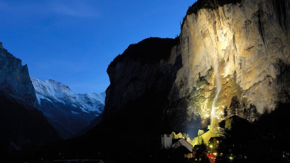 A mountain at dusk with a waterfall cascading down a cliff.