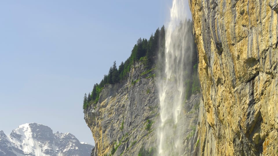 A waterfall cascading down a rocky cliff with snow-capped mountains in the background.