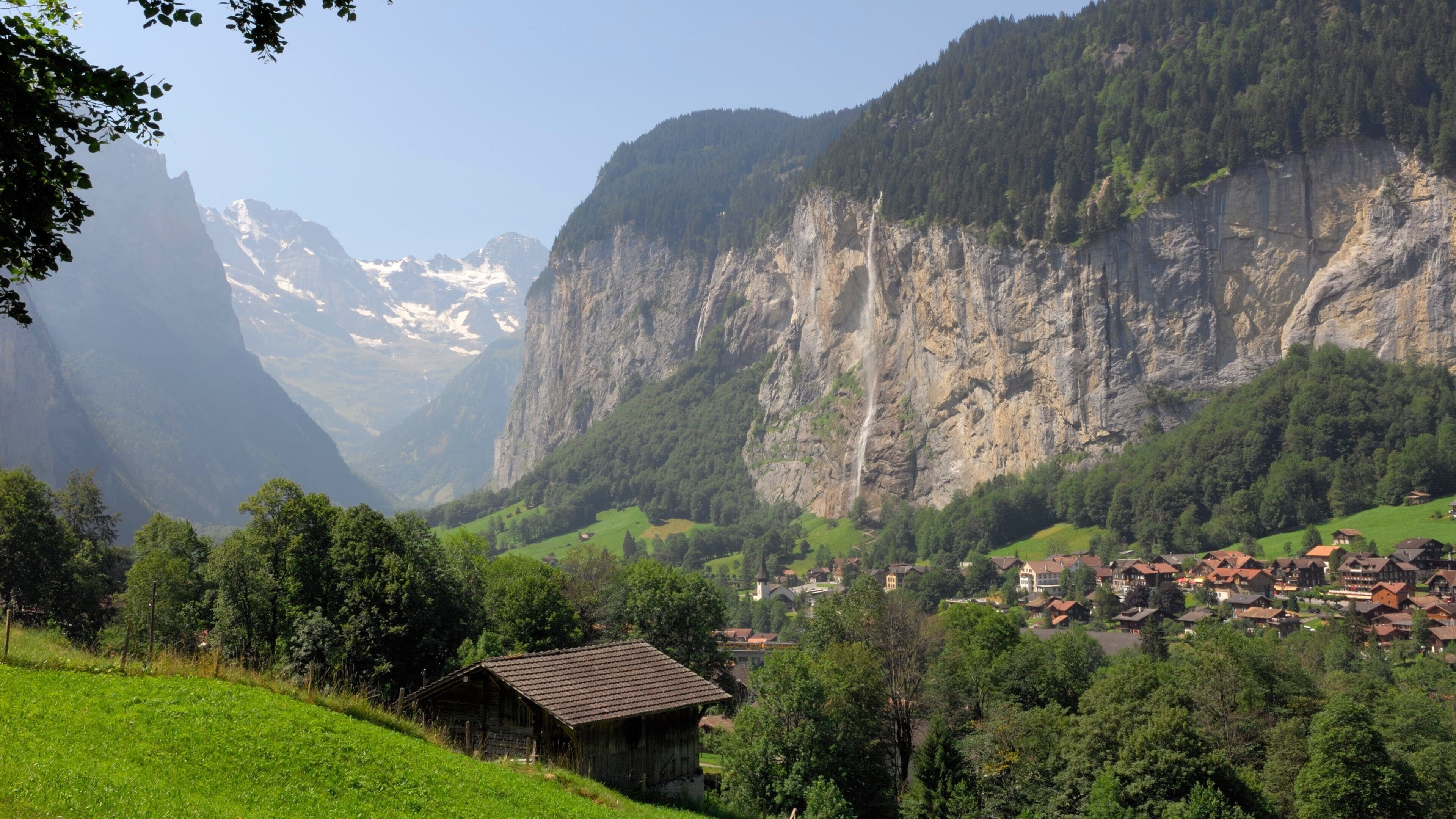 A mountainous landscape with a village nestled in a valley, surrounded by lush greenery and steep cliffs.