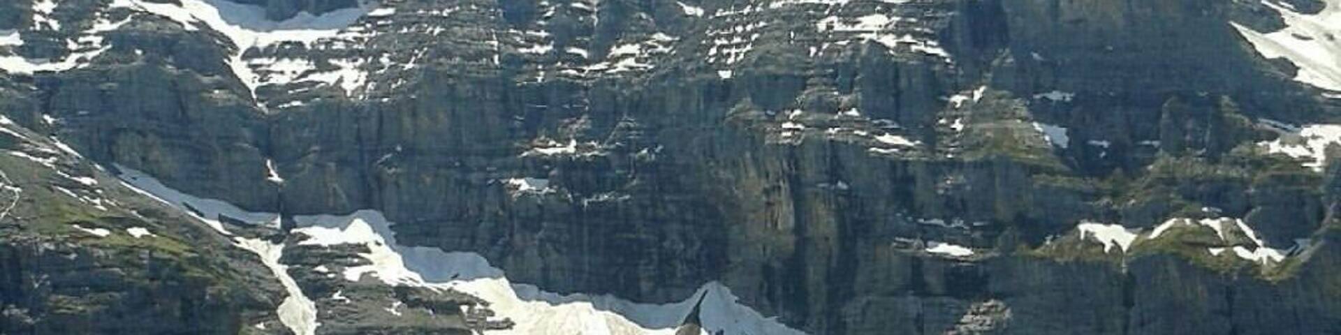 A mountain range with snow-capped peaks, a glacier, and a small settlement with houses.