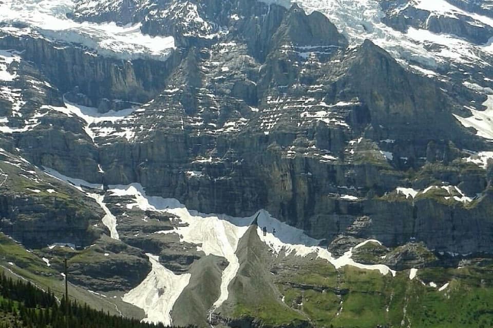 Une chaîne de montagnes aux sommets enneigés, un glacier et un petit village avec des maisons.