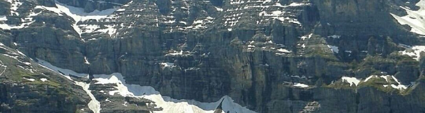 Cordilheira com picos nevados, uma geleira e um pequeno povoado com casas.
