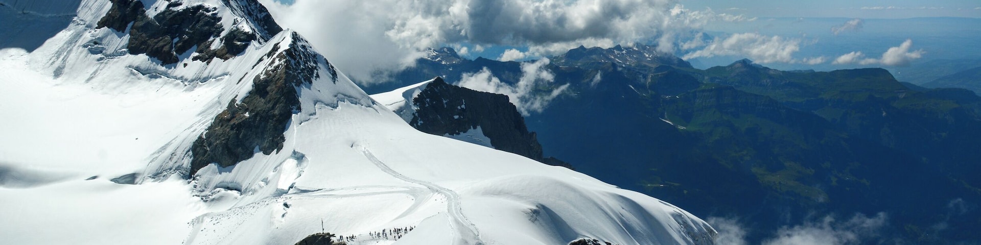 Un pico montañoso cubierto de nieve, con cielo despejado y nubes.