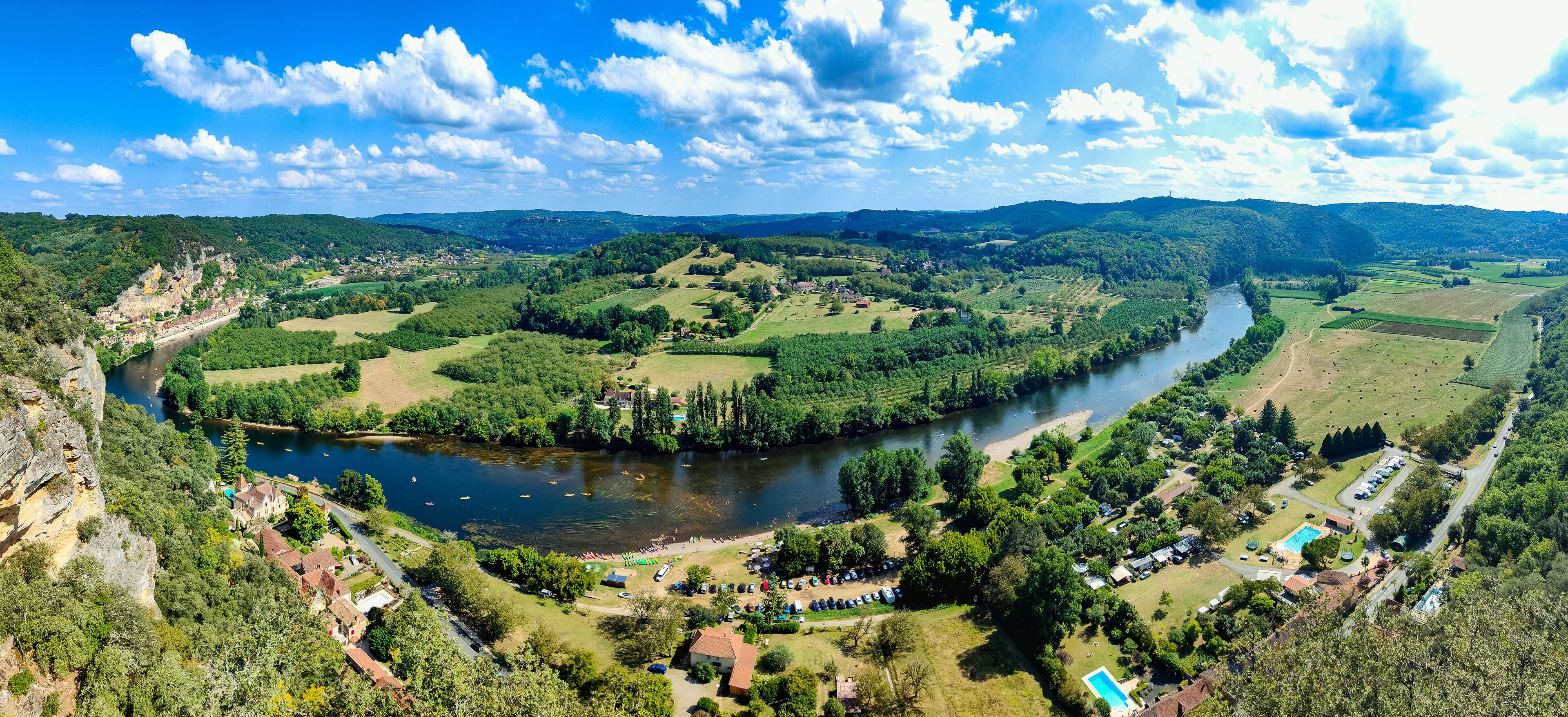A river winding through a valley with a castle on a hill, surrounded by greenery and fields.