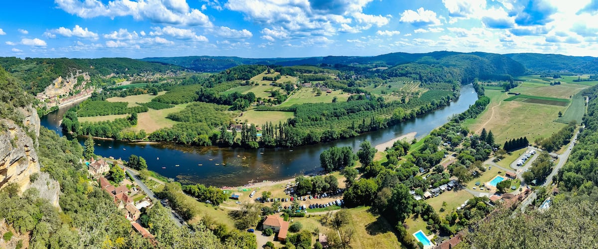 A river winding through a valley with a castle on a hill, surrounded by greenery and fields.