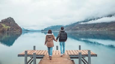 A wooden pier extending into a calm lake, surrounded by hills and a cloudy sky.