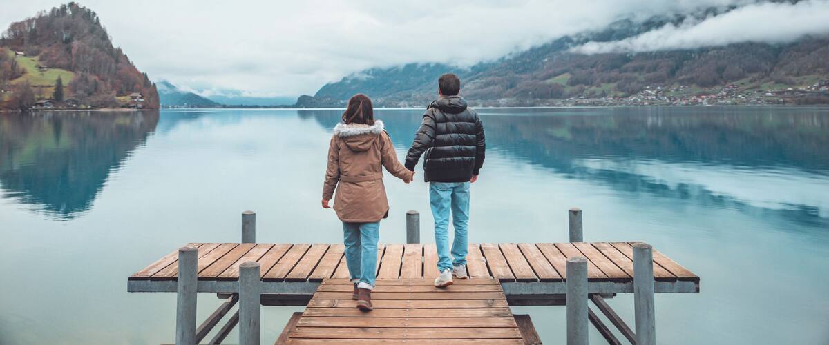 A wooden pier extending into a calm lake, surrounded by hills and a cloudy sky.