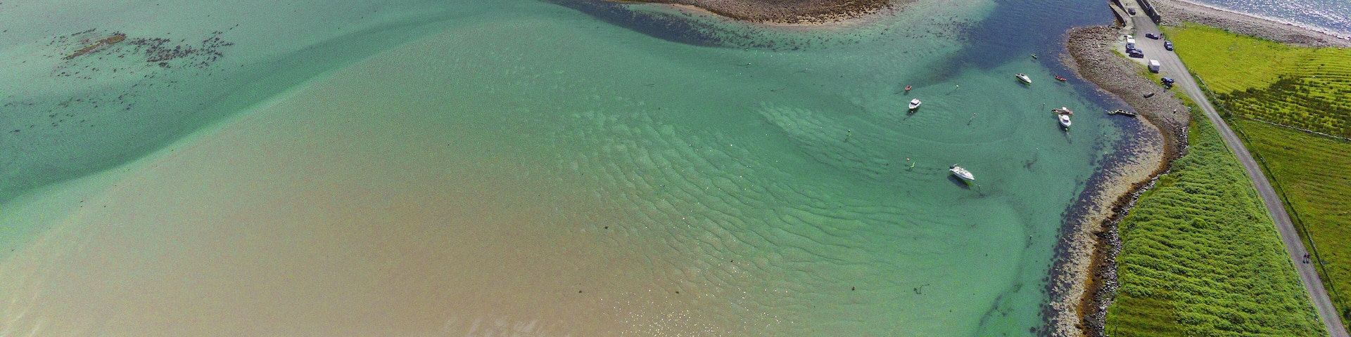 A coastal landscape with a sandy beach, clear turquoise waters, and a bridge connecting the land.