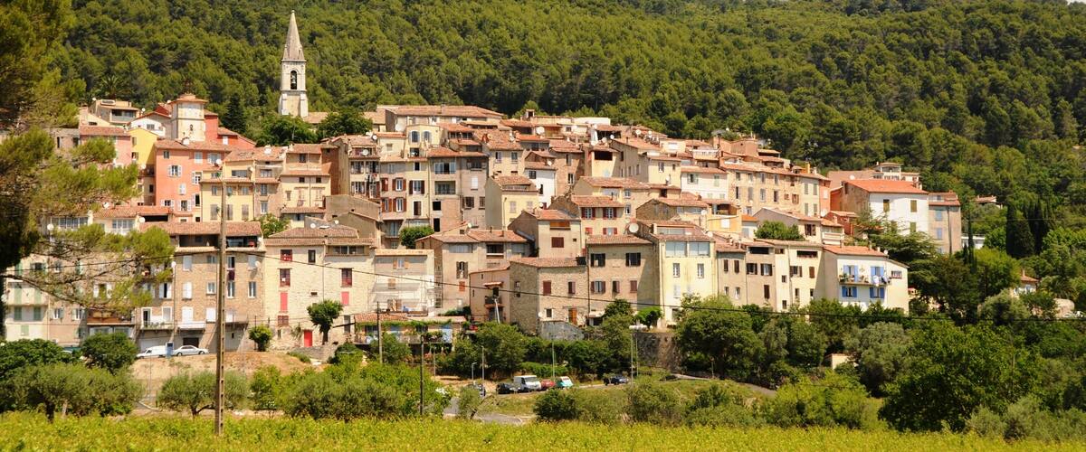 A hillside village with terracotta-roofed buildings, a church, and lush green hills in the background.