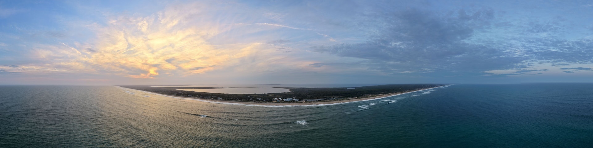 A coastal landscape with a beach, ocean waves, and a sunset sky.