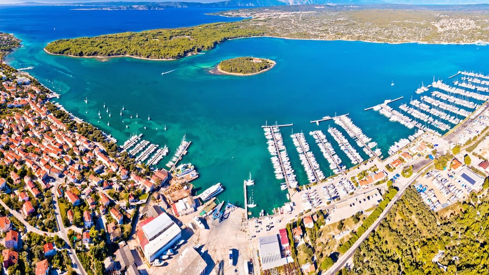 An aerial view of a coastal town with a marina, dense residential area, and a large body of water.