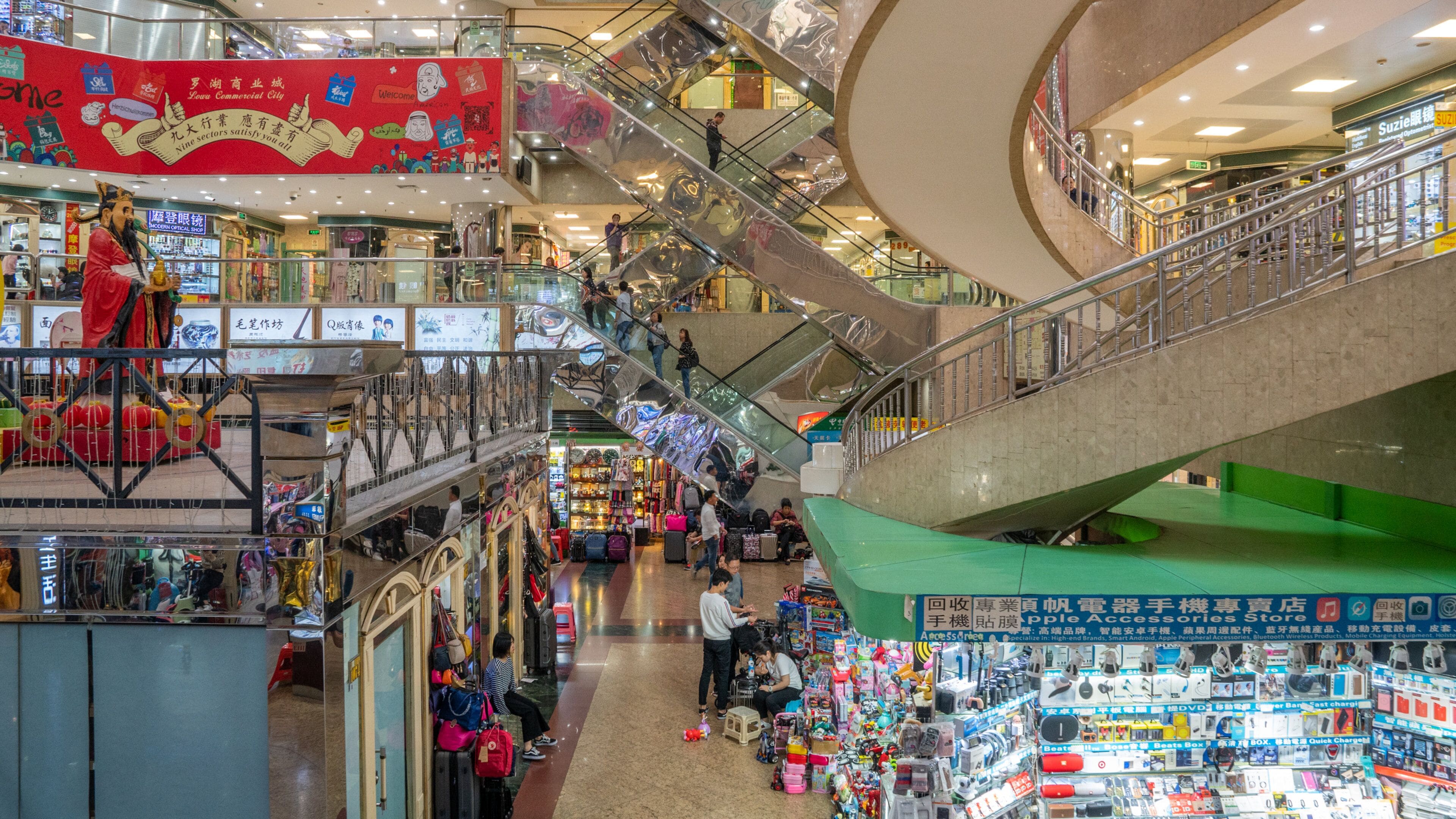 Een meerlaags winkelcentrum met roltrappen, diverse winkels en een opvallende rode banner.