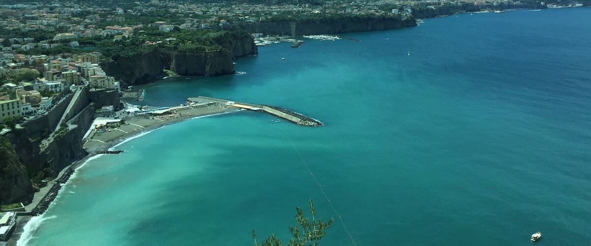 A coastal city with a prominent sea wall, a marina, and a mountainous backdrop.