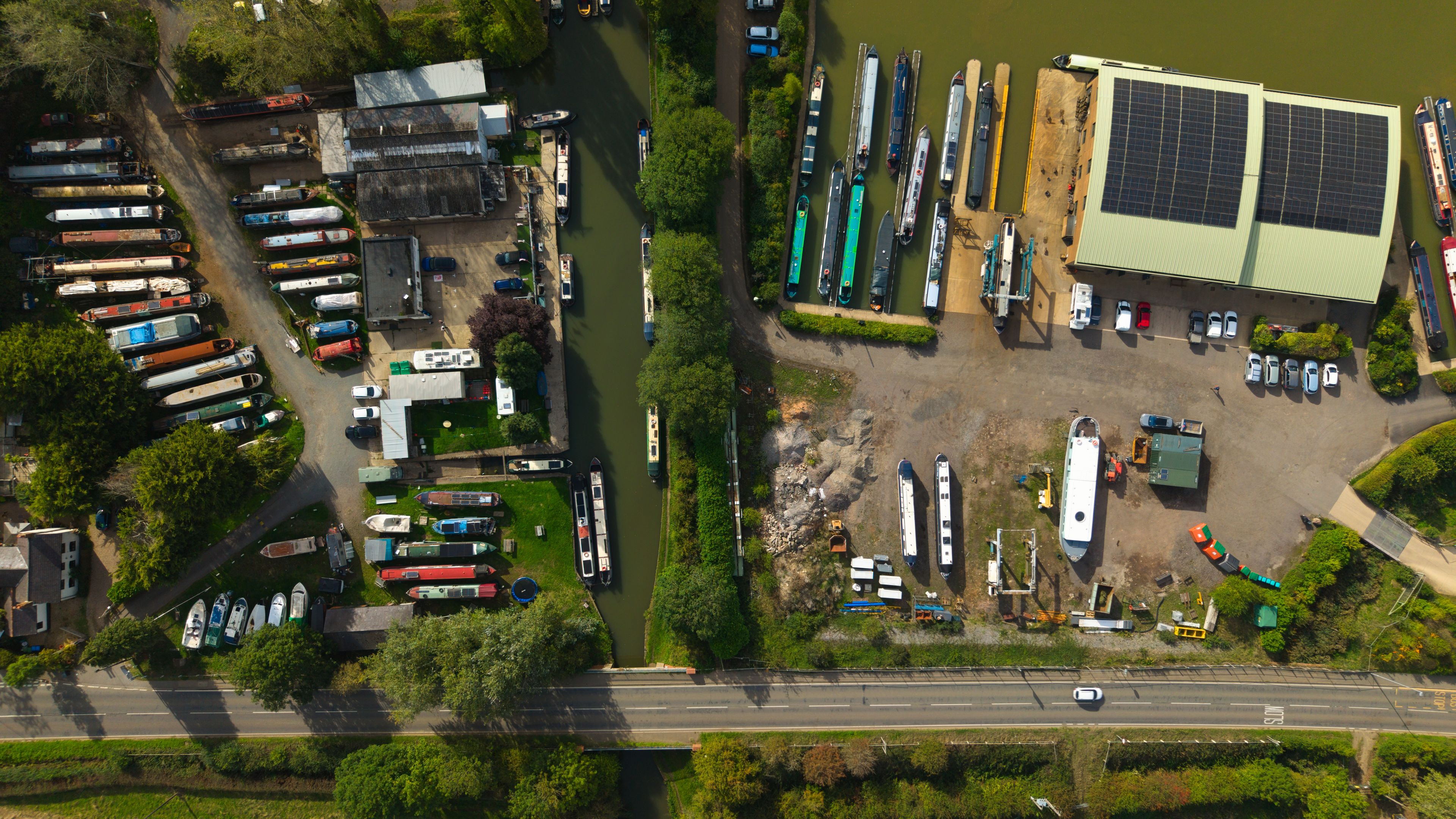 An aerial view of a marina with boats, a solar panel building, and a road.