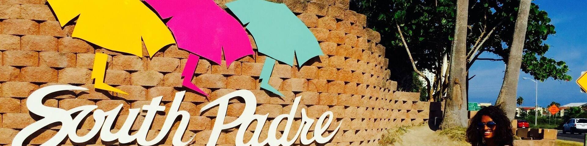 A sign for South Padre Island, Texas with colorful umbrellas and palm trees in the background.