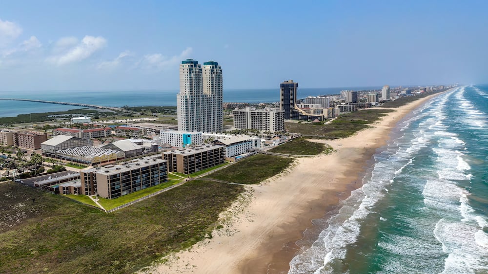 Eine Küstenstadt mit Strand, Hochhäusern und wolkenlosem, blauem Himmel.