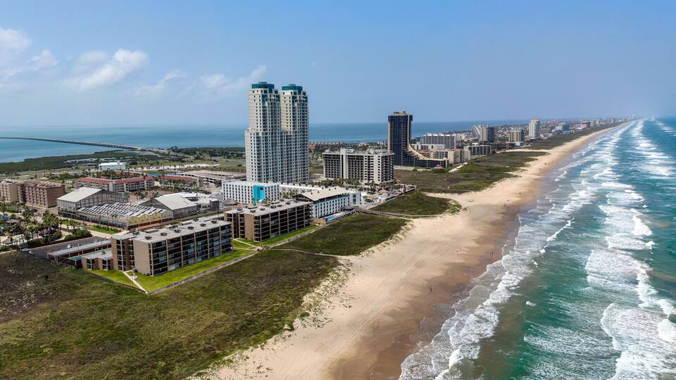 A coastal cityscape with a beach, high-rise buildings, and a clear blue sky.