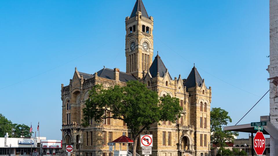 A historic building with a clock tower, a no left turn sign, and a stop sign.
