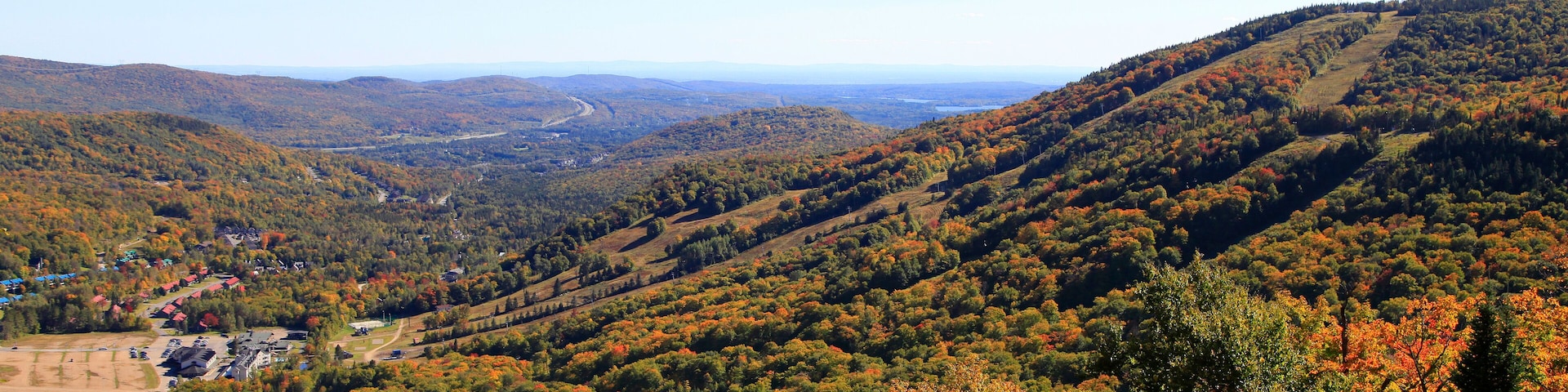 A valley with autumn foliage, a winding road, and scattered buildings.