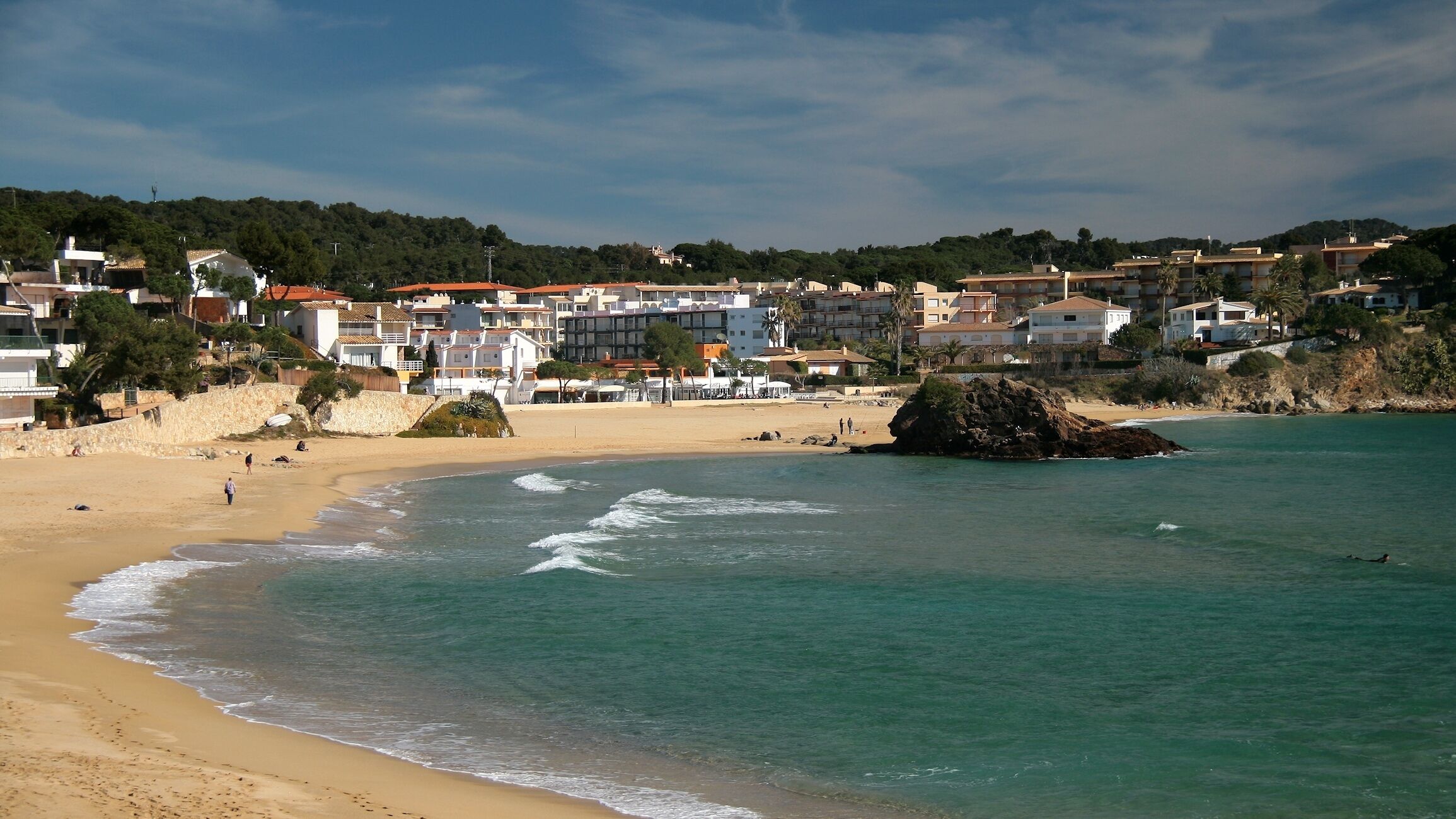 A coastal town with a sandy beach, turquoise waters, and buildings along the shore.