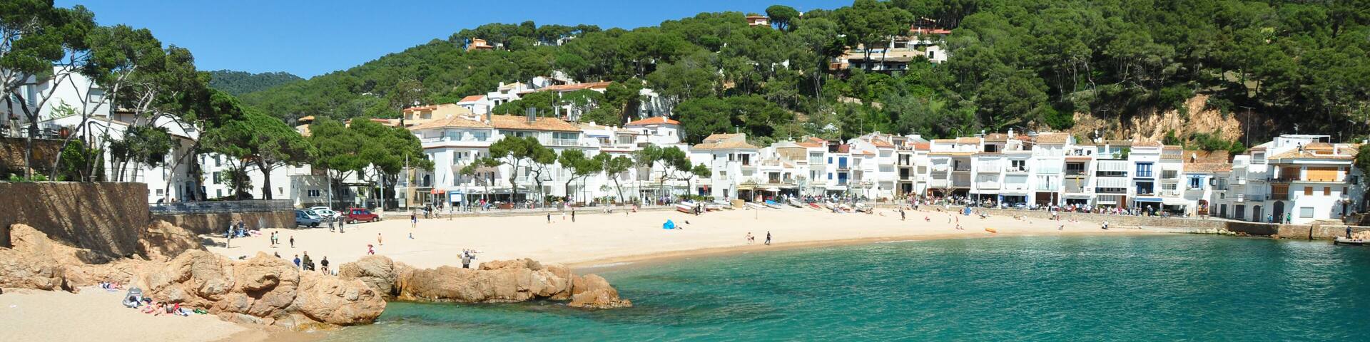 A coastal town with clear turquoise waters, sandy beach, and buildings on a hillside.