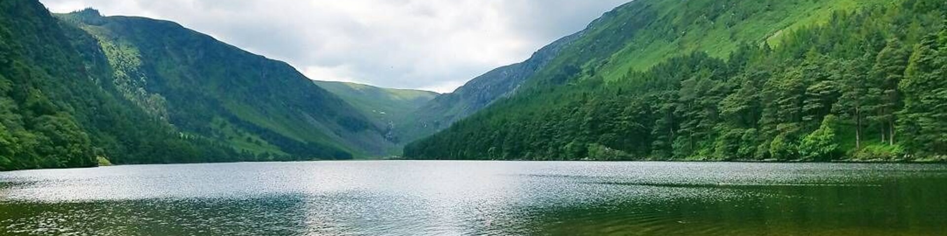 A lake surrounded by lush green hills under a cloudy sky.