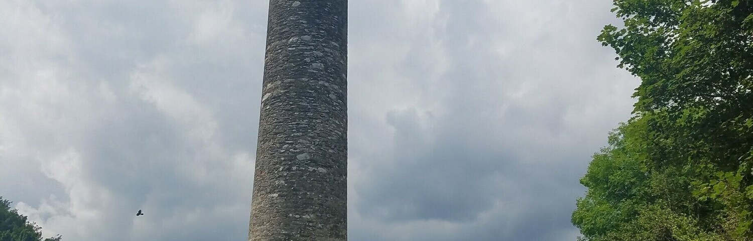 Una alta torre de piedra en un cementerio, con lápidas y un sendero que conduce a ella.
