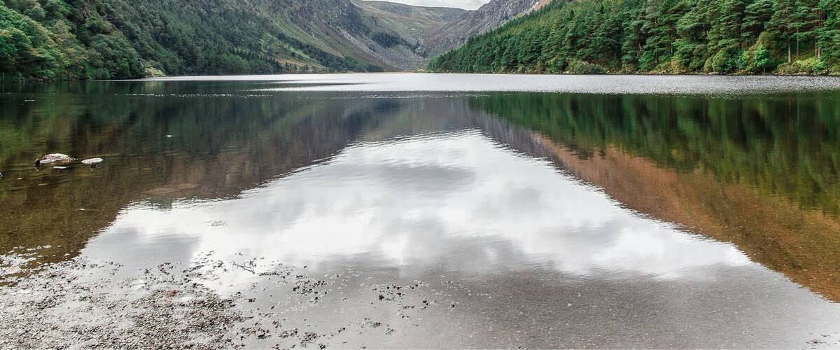 A calm lake surrounded by forested hills under a cloudy sky.