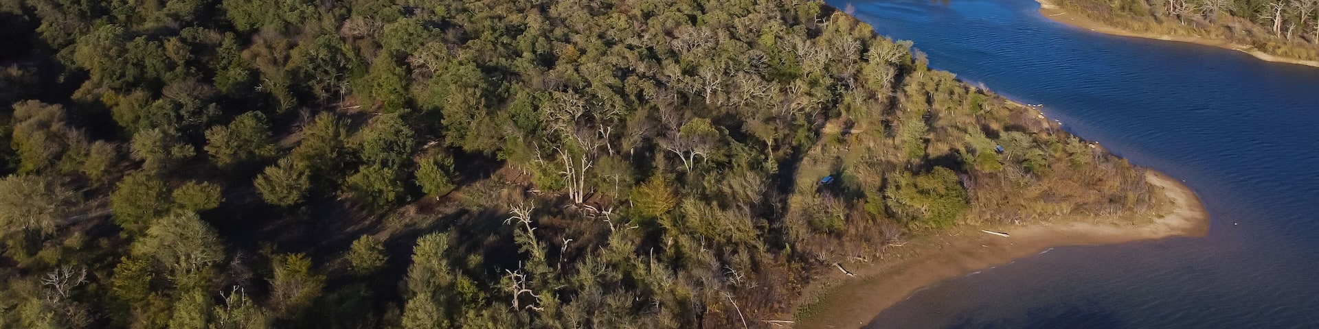 Aerial view a secondary point or hump surrounding by lush green trees and curved sandy shoreline at Isle du Bois Ray Roberts Lake State Park, remote primitive camping sites