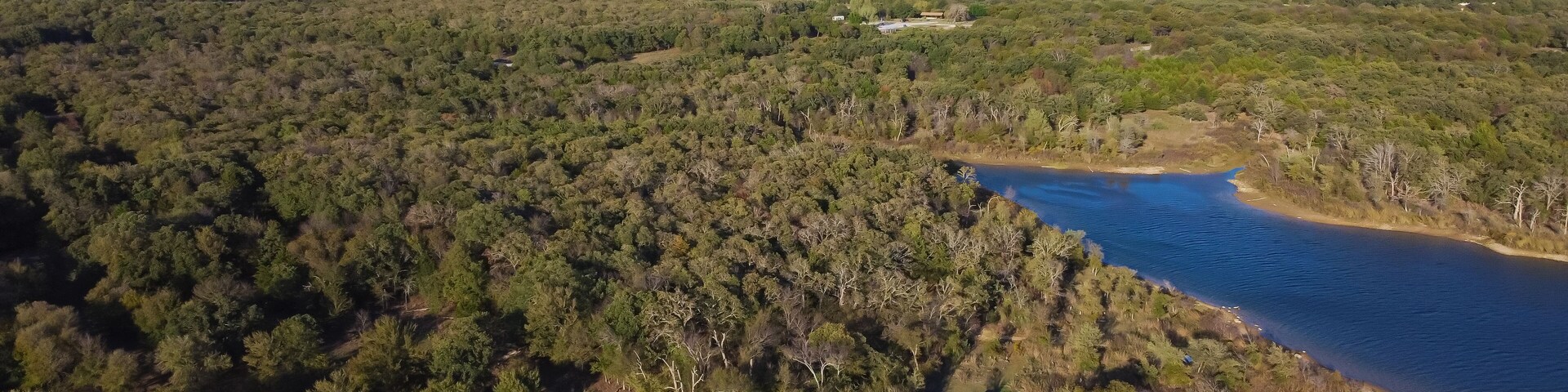 Aerial view a secondary point or hump surrounding by lush green trees and curved sandy shoreline at Isle du Bois Ray Roberts Lake State Park, remote primitive camping sites