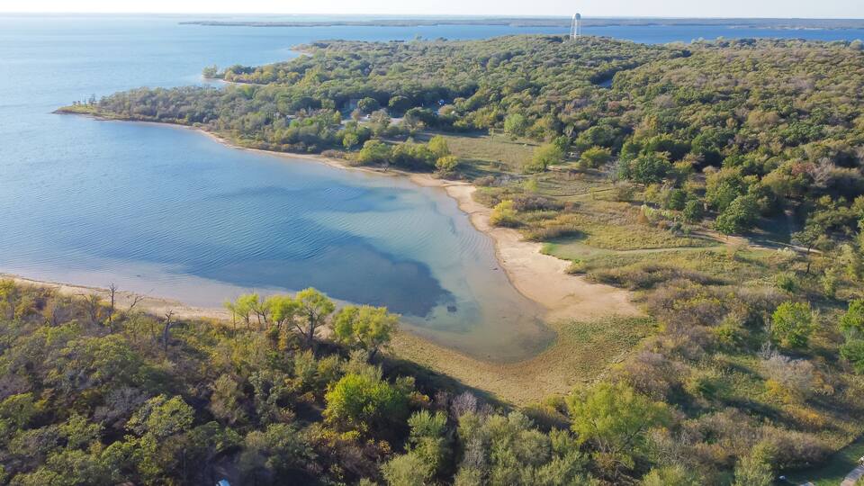 A coastal landscape with a sandy beach, dense greenery, and a water tower in the distance.