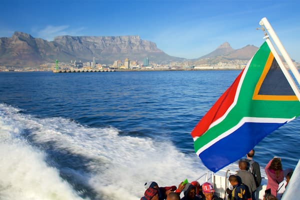 A boat with a South African flag, a cityscape with mountains in the background, and a clear blue sky.