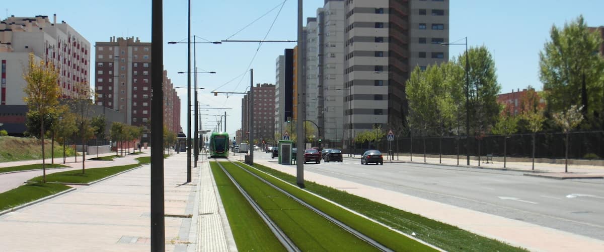 A modern urban street with tram tracks, green spaces, and high-rise buildings.