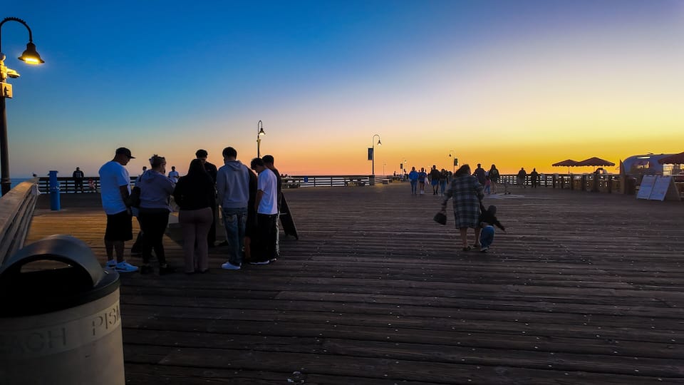 A wooden pier at sunset with people walking and standing.